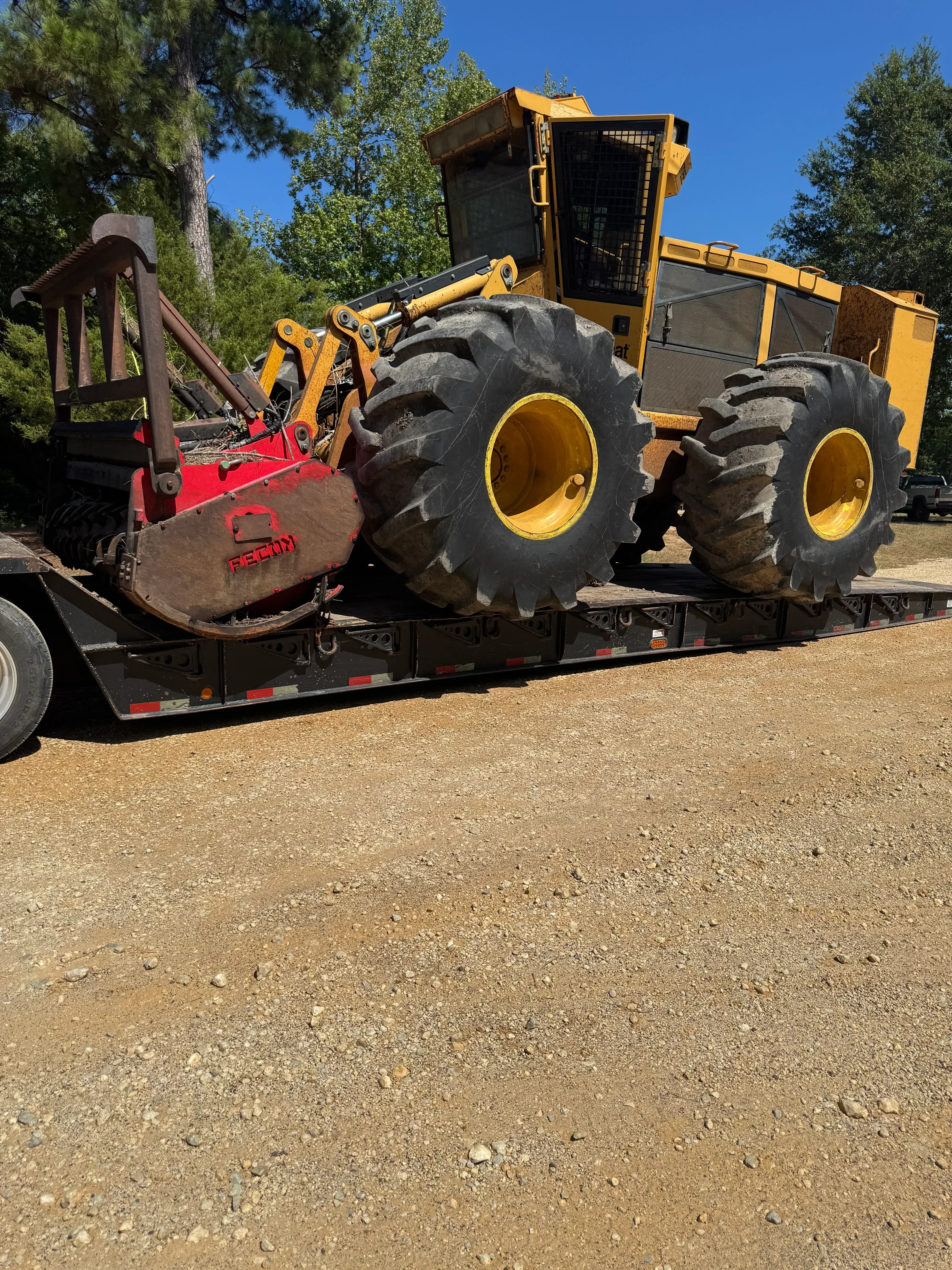 Yellow skid steer loader with red forestry mulcher on dirt road