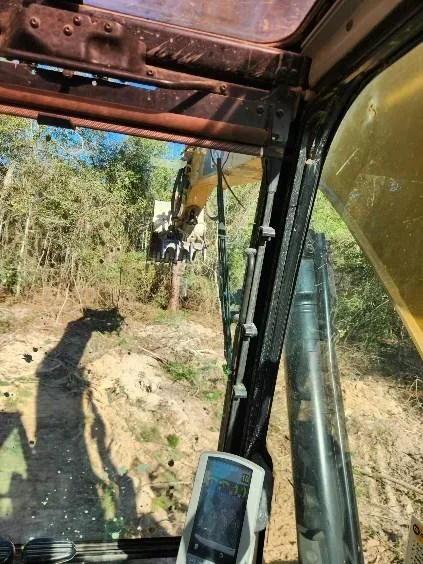 Excavator clearing trees and brush from wooded hillside with operator view from equipment cab